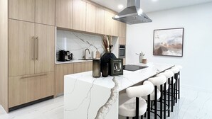 A modern kitchen with marble countertops, wooden cabinets, a central island with bar stools, and a stainless steel range hood. - Stylish comfortable villa. (Fort Lauderdale)