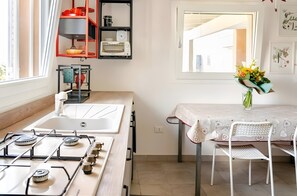 A kitchen with a gas stove, a sink, a window, and a dining area with a table and chairs. - Ruralholidays Experience in the Heart of Salento (Castri di Lecce)