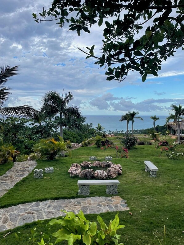 A lush garden with a stone pathway, a stone bench, and a view of the ocean. - 6 BR, 5 Bath Private Ocean & Jungle View Villa w/Pools (Las Terrenas)