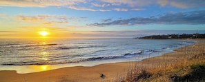 Una playa con un atardecer, mar tranquilo y costa lejana.