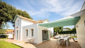 Et moderne hus med en træterrasse, en overdækket terrasse og en lille have.