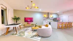 A modern living room with a sofa, a coffee table, a TV, and a dining area with chairs. - Walk to Broadway • 14 Beds • Pool/Hot Tub • Sauna! (Nashville)