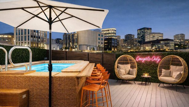 A rooftop bar with a pool, wicker furniture, and a city skyline view. - Walk to Broadway • 14 Beds • Pool/Hot Tub • Sauna! (Nashville)