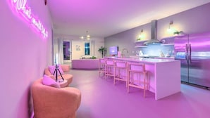 A modern kitchen with a bar area, a pink neon sign, and a seating area with a tripod. - Walk to Broadway • 14 Beds • Pool/Hot Tub • Sauna! (Nashville)