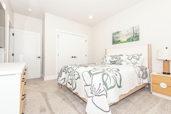 A bedroom with a bed, a dresser, a nightstand, a painting, and a door. - NEW Upscale Pet Friendly Condo - Walk to Outlets + Near Beaches (Rehoboth Beach)