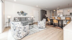 Ein modernes Wohnzimmer mit einer Couch, Sesseln, einem Couchtisch und einem Essbereich mit Stühlen und einem Tisch.