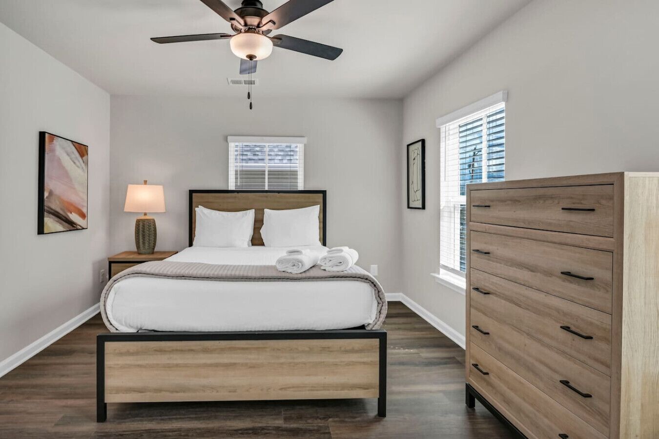 A bedroom with a bed, a nightstand, a dresser, a ceiling fan, and a window with blinds.
