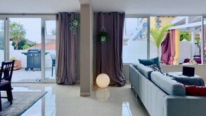 Ein modernes Wohnzimmer mit einem grauen Sofa, einem Esstisch und einem großen Fenster mit Vorhängen.