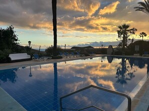 Una piscina con lettini e palme, circondata da un'area curata.