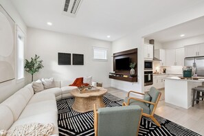 A modern living room with a sectional sofa, a round coffee table, and a TV mounted on the wall.