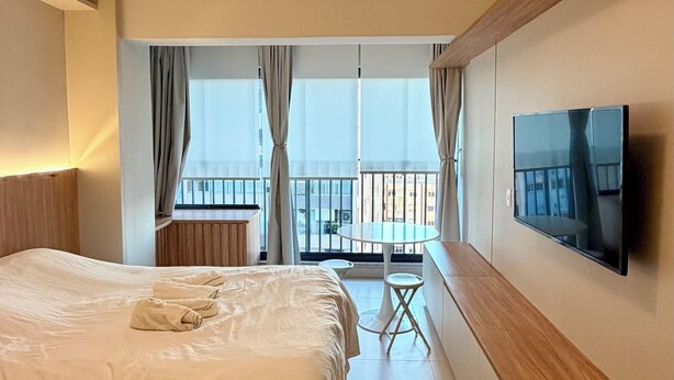 Ein modernes Hotelzimmer mit einem großen Bett, einem Flachbildfernseher, einem Balkon mit Tisch und Stühlen sowie Blick auf die Stadt.
