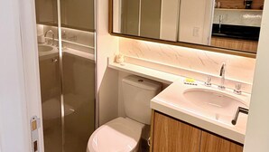 Ein modernes Badezimmer mit Duschkabine aus Glas, Toilette, Waschbecken und Spiegel über dem Waschtisch.