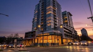 A multi-story building with a glass facade, a visible entrance, and a street view with cars and pedestrians. - West Coast City Living (Victoria)