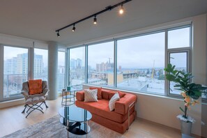 Ein modernes Wohnzimmer mit großem Fenster, einer Couch, einem Sessel und einem kleinen Tisch.