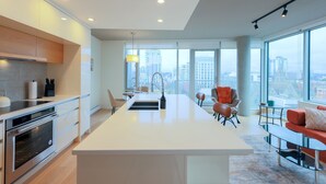 A modern kitchen with an island, dining area with chairs, and large windows offering a city view. - West Coast City Living (Victoria)