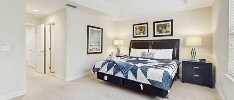 Un dormitorio con cama, mesitas de noche, cómoda y una puerta que da a otra habitación.