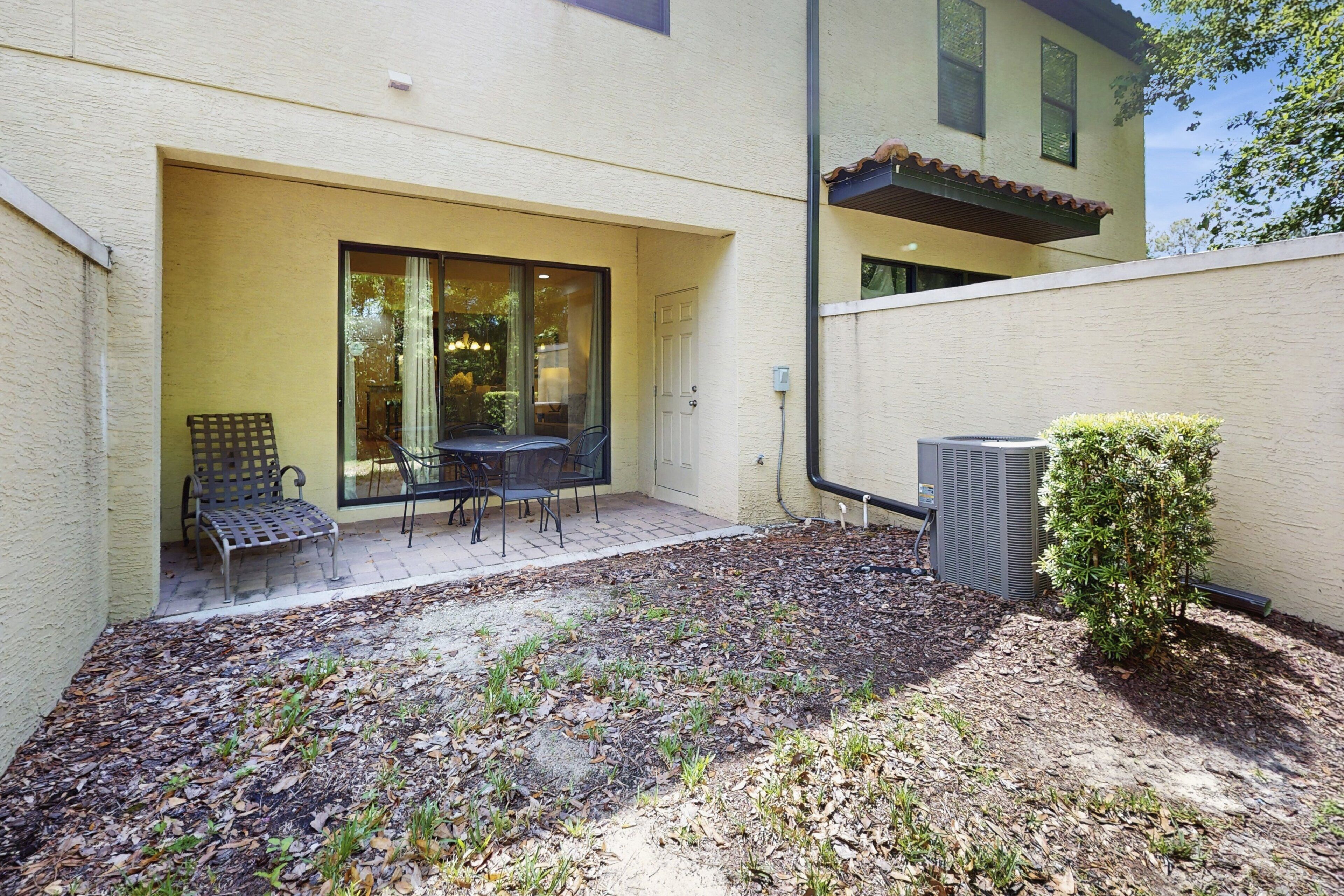 An outdoor patio with a table and chairs, a bench, and a small bush.