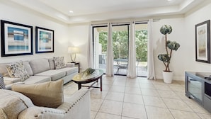 A living room with a sofa, coffee table, TV, and potted plants. - Gorgeous Snowbird-friendly Home With Pool, hot Tub, & gym - Close to Theme Parks (Davenport)