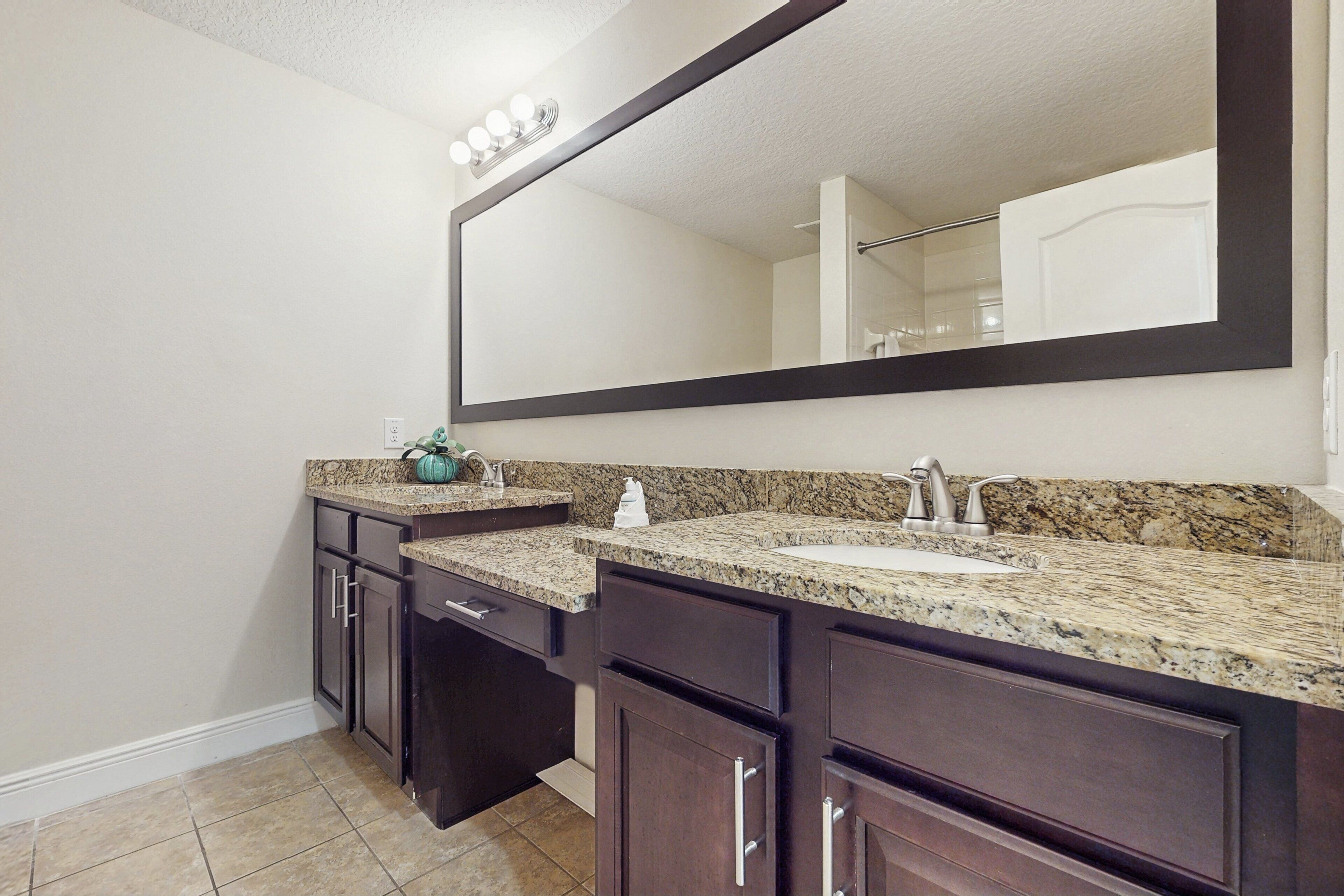 A bathroom with a large mirror, two sinks, dark cabinetry, and a granite countertop.
