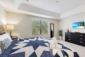 A bedroom with a large bed, a nightstand, a dresser, a TV, a window with blinds, and a mirror. - Gorgeous Snowbird-friendly Home With Pool, hot Tub, & gym - Close to Theme Parks (Davenport)