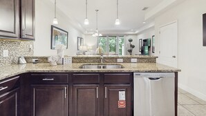 A modern kitchen with granite countertops, dark wood cabinets, a stainless steel sink, and a dishwasher. - Gorgeous Snowbird-friendly Home With Pool, hot Tub, & gym - Close to Theme Parks (Davenport)