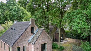 Une maison en briques avec un toit en pente, une petite dépendance attenante et un jardin agrémenté d’une table et de chaises.