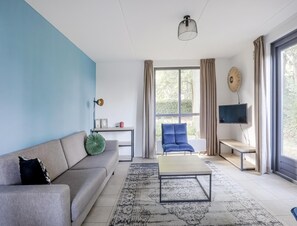 Ein modernes Wohnzimmer mit einer Couch, einem Couchtisch, einem Fernseher und großen Fenstern.