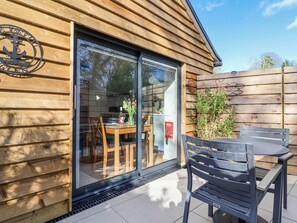Une cabane en bois dotée d’une porte-fenêtre coulissante qui donne sur un espace repas extérieur, avec une table et des chaises.