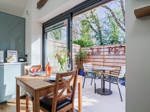A dining area with a wooden table and chairs, a glass window, and a wooden fence with 'LE P'tit' written on it. - Le Petit Glen (Lyme Regis)