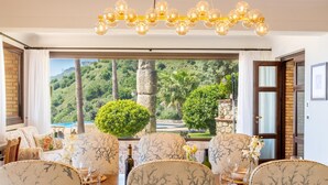A dining area with a view of lush greenery and a stone wall. - Villa Nerissa - Letojanni (Letojanni)