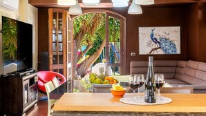Un soggiorno moderno con un tavolo da pranzo in legno, una sedia rossa e un divano. Si vede una televisione, un dipinto di un pavone e una ciotola di frutta sul tavolo.