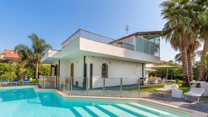 Una moderna casa a due piani con piscina, area relax esterna e palme.