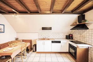 A kitchen with white cabinets, a dishwasher, an oven, and a wooden ceiling. - Gîte in Southern Alsace Largue – Peaceful Countryside Retreat (Wolfersdorf)