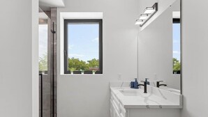 A modern bathroom with a large window, a white vanity with a mirror, and a glass shower enclosure. - Welcome to Blue Haven Retreat, beautifull 2- bedroom located in South St. Louis (St. Louis)