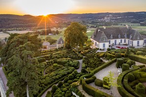 A landscaped garden with geometric hedges, a large tree, and a building with a steep roof. - DOMAINE6ha - EXCEPTIONAL VIEW OVER BEYNAC CASTELNAUD AND MARQUEYSSAC SWIMMING POOL 5X15 (Vézac)
