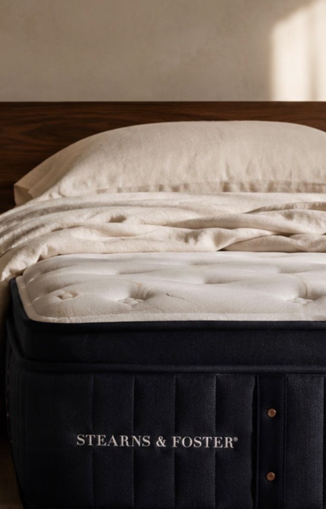 Una cama con cabecera oscura y una almohada. El cubre cama es blanco.