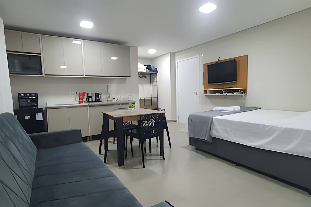 A compact room with a sofa, a small table, a kitchenette, a TV, and a bed.