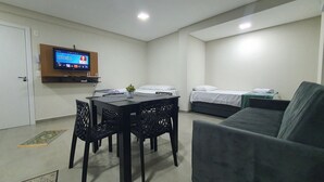 Ein Zimmer mit Esstisch, Stühlen, einer Couch, einem an der Wand befestigten Fernseher und einem Bett.