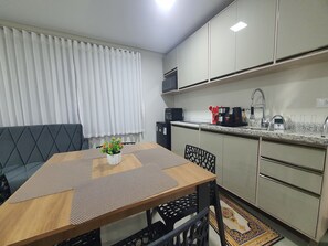 Una cocina compacta con comedor, que incluye microondas, estufa, lavaplatos y una planta en maceta sobre la mesa.