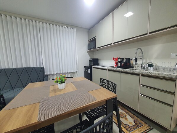 Une cuisine compacte avec un coin repas, comprenant un four à micro-ondes, une cuisinière, un évier et une plante en pot posée sur la table.
