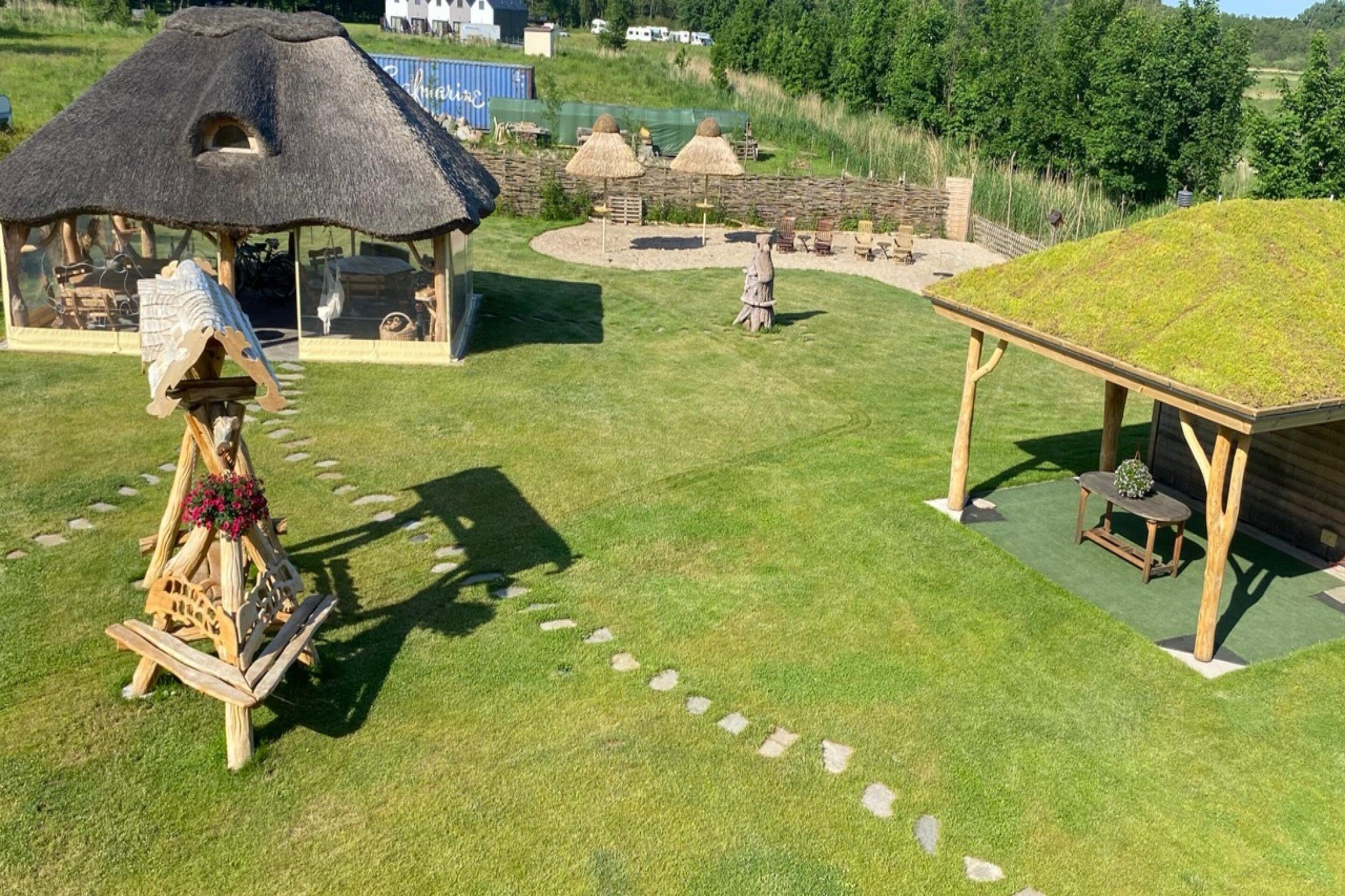 A thatched-roof structure with a wooden bench and a table, surrounded by a well-maintained lawn and a stone wall.