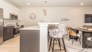 Et moderne køkken med en central ø, rustfrie stålapparater samt et spiseområde med stole og et bord.