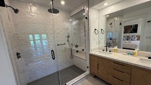 Uma casa de banho moderna com chuveiro envidraçado, um espelho grande e toucador com bancada.