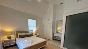 Quarto com cama, mesas de cabeceira, guarda-roupa, espelho e uma janela grande.