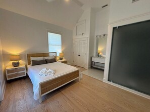 Ein Schlafzimmer mit einem Bett, Nachttischen, einem Kleiderschrank, einem Spiegel und einem großen Fenster.