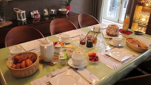 Een eettafel gedekt met borden, kopjes en een mandje gebak.