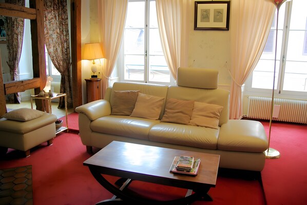 A living room with a sofa, a coffee table, a lamp, and a window with curtains. - Cour Du Weinhof - Bartholdi Room with Shared Terrace and Wi-Fi (Colmar)