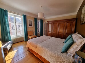 A bedroom with a bed, wooden wardrobe, a small table, and a window with curtains.