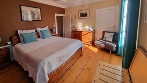 Een slaapkamer met een houten bed, een nachtkastje, een kapstok, een lamp en een deur.