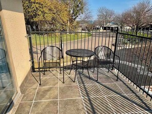 Een balkon met een metalen hek, twee stoelen en een kleine tafel.